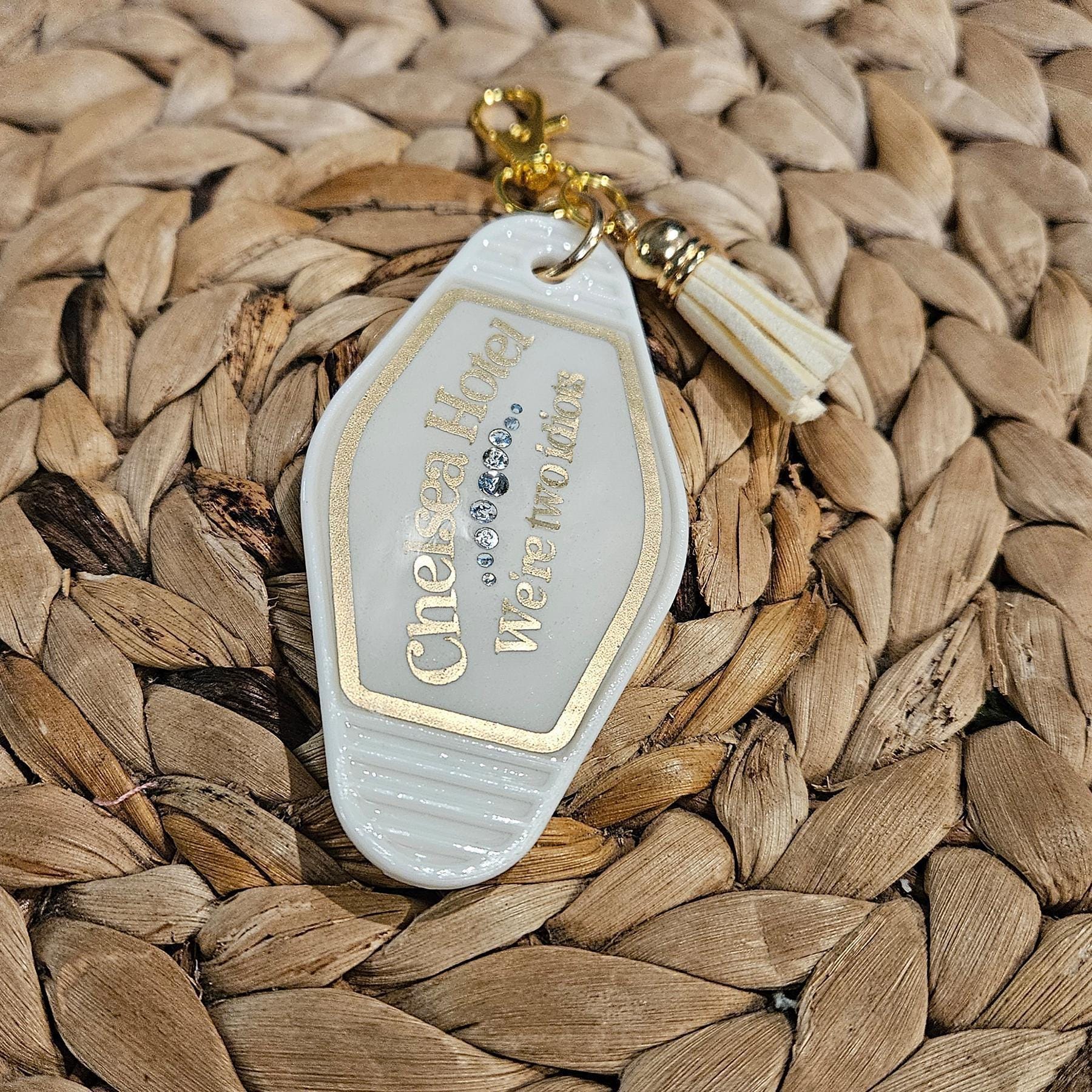 Embrace the brooding romance and moody nostalgia of the legendary Chelsea Hotel aesthetic with this vintage-inspired motel keychain. Perfect for the poetic souls, late-night writers, and lovers of timeless, slightly dramatic flair. Featuring the slightly tragic yet entirely relatable phrase "We're two idiots" in sleek matte gold vinyl, it is a nod to those beautifully chaotic moments shared between fellow creatives, book nerds, and star-crossed friends. Product Details: - Vintage Appeal: Gorgeou (3)