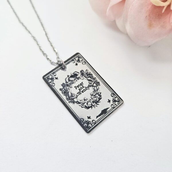 Engraved Peter and Wendy Book Necklace – Stainless Steel Literary Jewelry 4 Miniature Peter and Wendy book pendant, engraved in-house with original cover art. Mirror-polish stainless steel, tarnish-proof. A gift for every lost girl. “To live would be an awfully big adventure.” ✨🧚♂️ Fly away to Neverland with a piece of jewelry as unique as the story itself. Our Peter and Wendy Book Necklace features original cover art designed in our studio, making this a one-of-a-kind tribute you won't find anywhere else. Forget mass-produced charms. Each pendant is engraved in-house (4)
