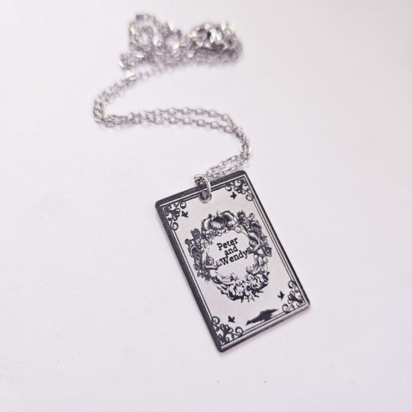 Engraved Peter and Wendy Book Necklace – Stainless Steel Literary Jewelry 6 Miniature Peter and Wendy book pendant, engraved in-house with original cover art. Mirror-polish stainless steel, tarnish-proof. A gift for every lost girl. “To live would be an awfully big adventure.” ✨🧚♂️ Fly away to Neverland with a piece of jewelry as unique as the story itself. Our Peter and Wendy Book Necklace features original cover art designed in our studio, making this a one-of-a-kind tribute you won't find anywhere else. Forget mass-produced charms. Each pendant is engraved in-house (6)