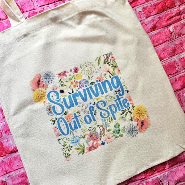 For the fiercely independent friend who thrives on proving people wrong! 💐 Give the gift of unapologetic resilience with this Surviving Out of Spite tote bag. Why this tote stands on business: 💼 Permanent Design: The design is sublimated. The ink is dyed directly into the fibers, meaning it won’t fade, rub off, or lose its punch—no matter how many times you wash it. 🧼✨ Premium Build: Made from high-quality, medium-weight cotton canvas. It’s sturdy enough for your laptop, your protest signs, or a (4)