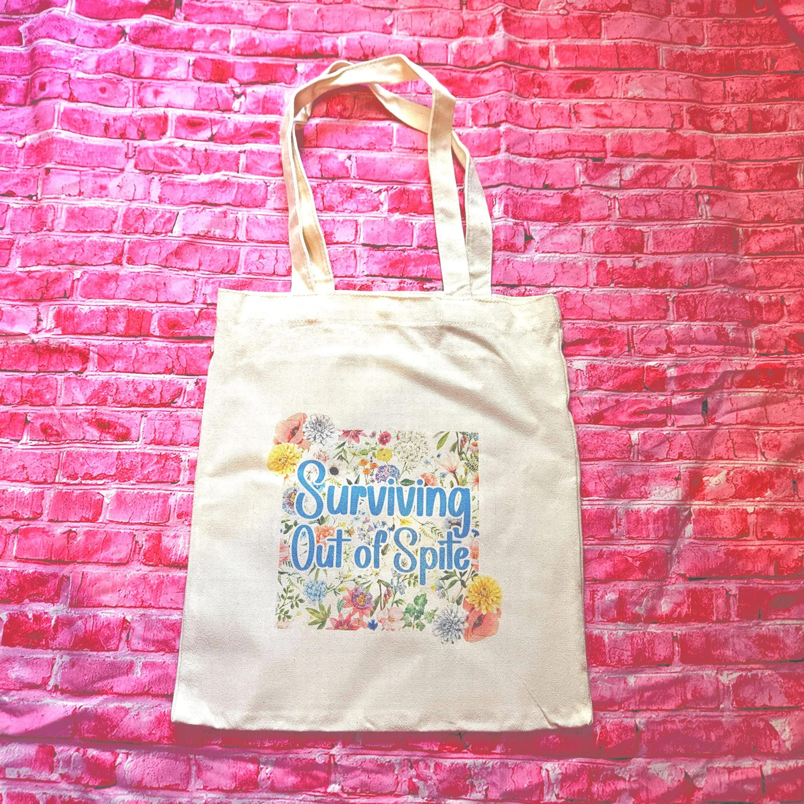 For the fiercely independent friend who thrives on proving people wrong! 💐 Give the gift of unapologetic resilience with this Surviving Out of Spite tote bag. Why this tote stands on business: 💼 Permanent Design: The design is sublimated. The ink is dyed directly into the fibers, meaning it won’t fade, rub off, or lose its punch—no matter how many times you wash it. 🧼✨ Premium Build: Made from high-quality, medium-weight cotton canvas. It’s sturdy enough for your laptop, your protest signs, or a (2)