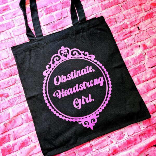 Jane Austen Tote Bag - Obstinate Headstrong Girl Canvas Book Bag 3 The ultimate gift for the witty bookworm! 📚 This bold Jane Austen tote bag features the "Obstinate Headstrong Girl" quote. Perfect for library hauls and gifts. Obsessed with Jane Austen but tired of boring, beige book bags? We’ve got you. This She’sSoCrafty Goods original design takes the wit of Pride and Prejudice and gives it a bold, modern glow-up. 💖✨ Crafted from premium, heavyweight black cotton canvas, this 14" x 15" tote is sturdy enough to carry your entire TBR (To-Be-Read) pile, your la (3)