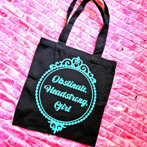 Jane Austen Tote Bag - Obstinate Headstrong Girl Canvas Book Bag 4 The ultimate gift for the witty bookworm! 📚 This bold Jane Austen tote bag features the "Obstinate Headstrong Girl" quote. Perfect for library hauls and gifts. Obsessed with Jane Austen but tired of boring, beige book bags? We’ve got you. This She’sSoCrafty Goods original design takes the wit of Pride and Prejudice and gives it a bold, modern glow-up. 💖✨ Crafted from premium, heavyweight black cotton canvas, this 14" x 15" tote is sturdy enough to carry your entire TBR (To-Be-Read) pile, your la (4)