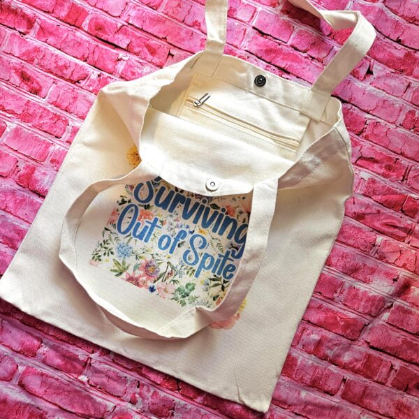 For the fiercely independent friend who thrives on proving people wrong! 💐 Give the gift of unapologetic resilience with this Surviving Out of Spite tote bag. Why this tote stands on business: 💼 Permanent Design: The design is sublimated. The ink is dyed directly into the fibers, meaning it won’t fade, rub off, or lose its punch—no matter how many times you wash it. 🧼✨ Premium Build: Made from high-quality, medium-weight cotton canvas. It’s sturdy enough for your laptop, your protest signs, or a (8)