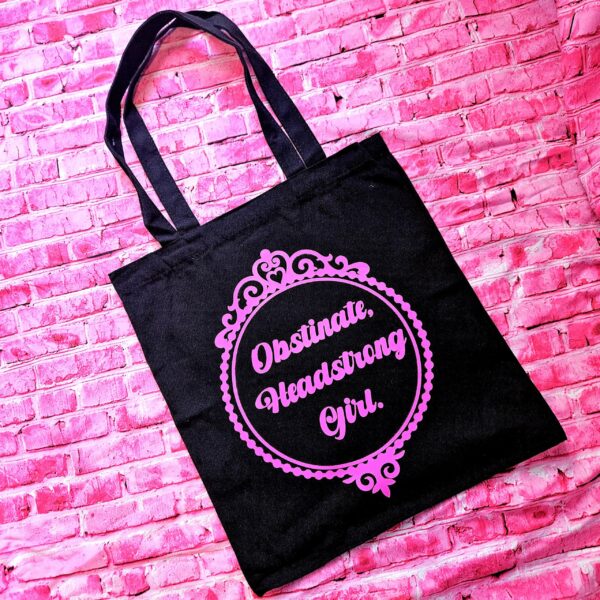 Jane Austen Tote Bag - Obstinate Headstrong Girl Canvas Book Bag 2 The ultimate gift for the witty bookworm! 📚 This bold Jane Austen tote bag features the "Obstinate Headstrong Girl" quote. Perfect for library hauls and gifts. Obsessed with Jane Austen but tired of boring, beige book bags? We’ve got you. This She’sSoCrafty Goods original design takes the wit of Pride and Prejudice and gives it a bold, modern glow-up. 💖✨ Crafted from premium, heavyweight black cotton canvas, this 14" x 15" tote is sturdy enough to carry your entire TBR (To-Be-Read) pile, your la (2)