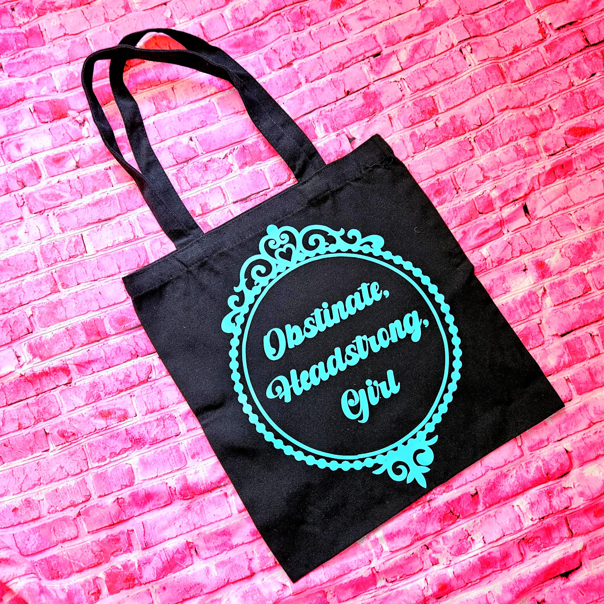 The ultimate gift for the witty bookworm! 📚 This bold Jane Austen tote bag features the "Obstinate Headstrong Girl" quote. Perfect for library hauls and gifts. Obsessed with Jane Austen but tired of boring, beige book bags? We’ve got you. This She’sSoCrafty Goods original design takes the wit of Pride and Prejudice and gives it a bold, modern glow-up. 💖✨ Crafted from premium, heavyweight black cotton canvas, this 14" x 15" tote is sturdy enough to carry your entire TBR (To-Be-Read) pile, your la (6)