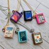 Custom Miniature Book Necklace, Personalized Book Lover Gift, Bookish Jewelry 4 Send us the link, we'll make it tiny. Your favorite book cover, shrunk to charm-sized perfection and hung around your neck. This custom miniature book necklace is a personalized book lover gift — handmade bookish jewelry featuring a 3D printed mini book pendant with hand-gilded pages and an 18" stainless steel chain. ✦ Pendant size: .85" H × .75" W ✦ Construction: 100% handmade and 3D printed from an original SSC design — never mass produced ✦ Cover: Printed from your chosen image, laminated for (4)