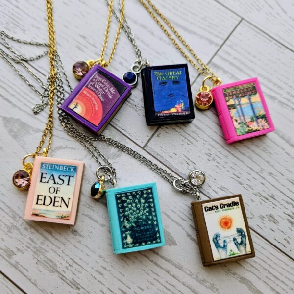 Custom Miniature Book Necklace, Personalized Book Lover Gift, Bookish Jewelry 4 Send us the link, we'll make it tiny. Your favorite book cover, shrunk to charm-sized perfection and hung around your neck. This custom miniature book necklace is a personalized book lover gift — handmade bookish jewelry featuring a 3D printed mini book pendant with hand-gilded pages and an 18" stainless steel chain. ✦ Pendant size: .85" H × .75" W ✦ Construction: 100% handmade and 3D printed from an original SSC design — never mass produced ✦ Cover: Printed from your chosen image, laminated for (4)
