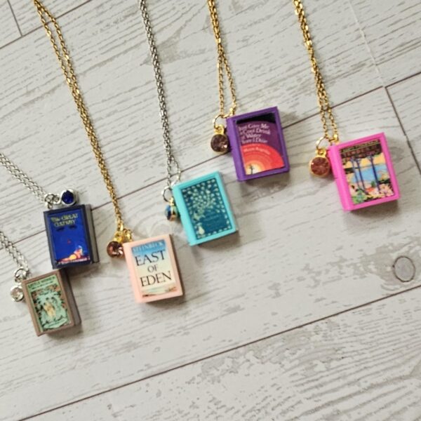 Custom Miniature Book Necklace, Personalized Book Lover Gift, Bookish Jewelry 3 Send us the link, we'll make it tiny. Your favorite book cover, shrunk to charm-sized perfection and hung around your neck. This custom miniature book necklace is a personalized book lover gift — handmade bookish jewelry featuring a 3D printed mini book pendant with hand-gilded pages and an 18" stainless steel chain. ✦ Pendant size: .85" H × .75" W ✦ Construction: 100% handmade and 3D printed from an original SSC design — never mass produced ✦ Cover: Printed from your chosen image, laminated for (3)