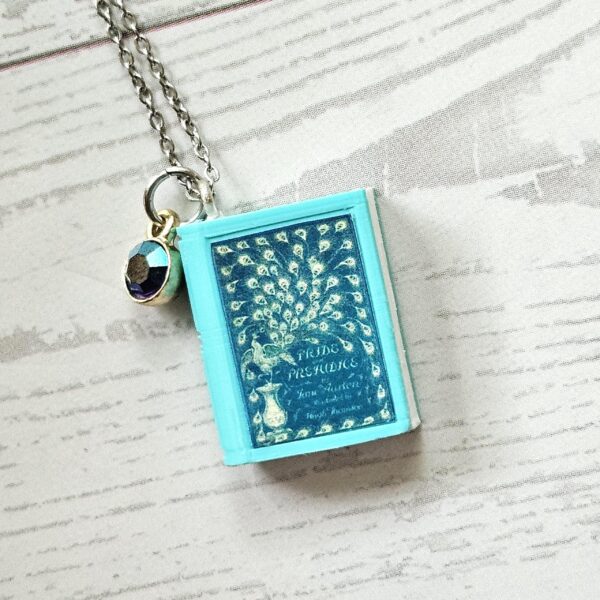 Custom Miniature Book Necklace, Personalized Book Lover Gift, Bookish Jewelry 5 Send us the link, we'll make it tiny. Your favorite book cover, shrunk to charm-sized perfection and hung around your neck. This custom miniature book necklace is a personalized book lover gift — handmade bookish jewelry featuring a 3D printed mini book pendant with hand-gilded pages and an 18" stainless steel chain. ✦ Pendant size: .85" H × .75" W ✦ Construction: 100% handmade and 3D printed from an original SSC design — never mass produced ✦ Cover: Printed from your chosen image, laminated for (5)