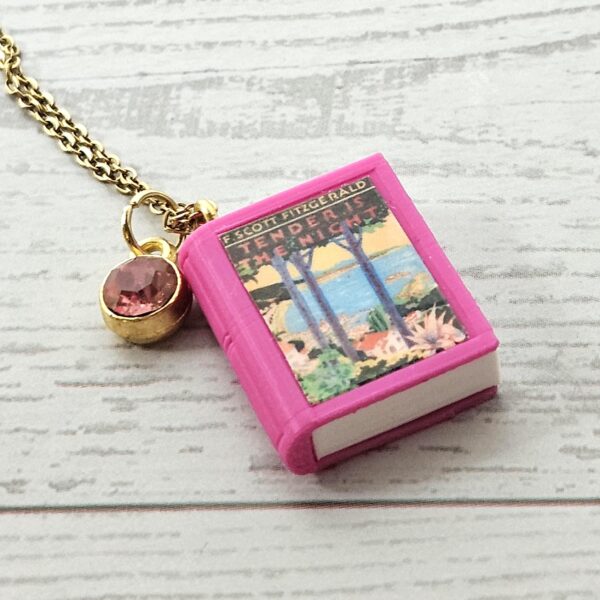 Custom Miniature Book Necklace, Personalized Book Lover Gift, Bookish Jewelry 6 Send us the link, we'll make it tiny. Your favorite book cover, shrunk to charm-sized perfection and hung around your neck. This custom miniature book necklace is a personalized book lover gift — handmade bookish jewelry featuring a 3D printed mini book pendant with hand-gilded pages and an 18" stainless steel chain. ✦ Pendant size: .85" H × .75" W ✦ Construction: 100% handmade and 3D printed from an original SSC design — never mass produced ✦ Cover: Printed from your chosen image, laminated for (6)